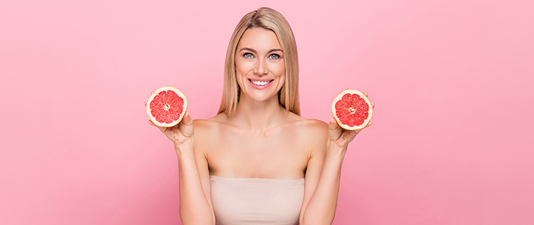 Smaidīga sieviete ar sagriezto greipfrūtu rokās